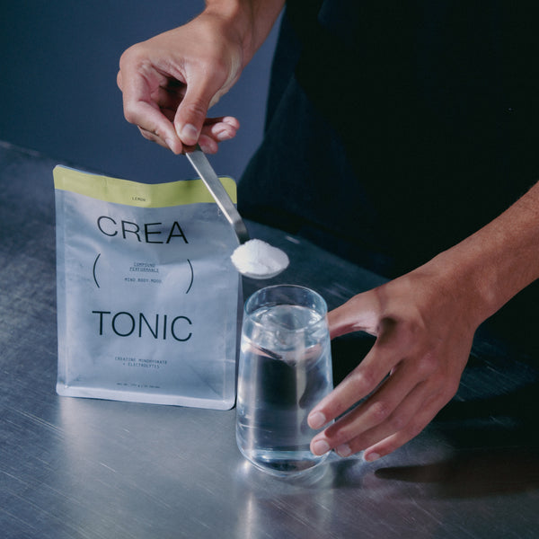Person adding creatine from a creatonic pouch into a glass of water on a dark surface.