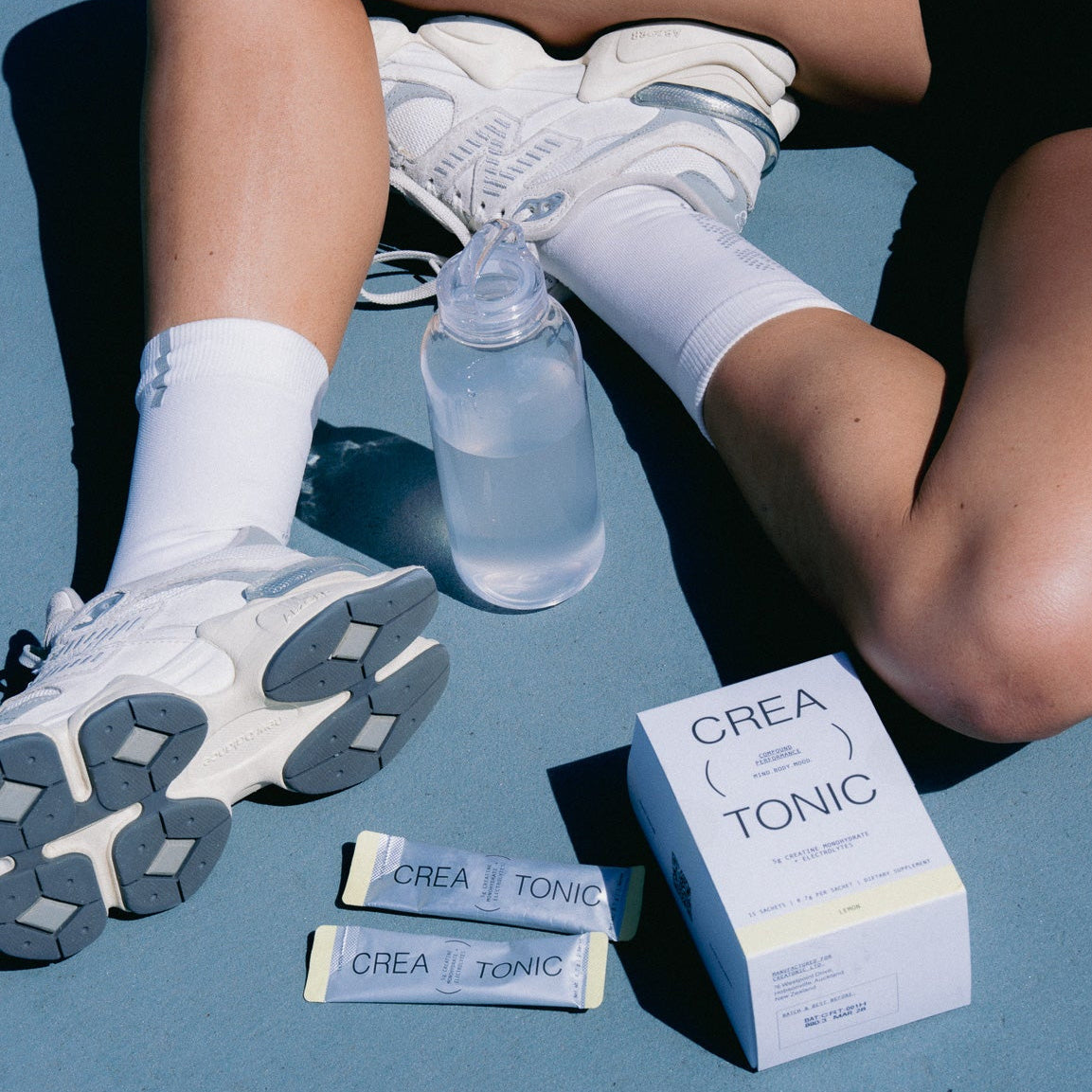 Person sitting on a blue surface with Creatonic products and a water bottle.